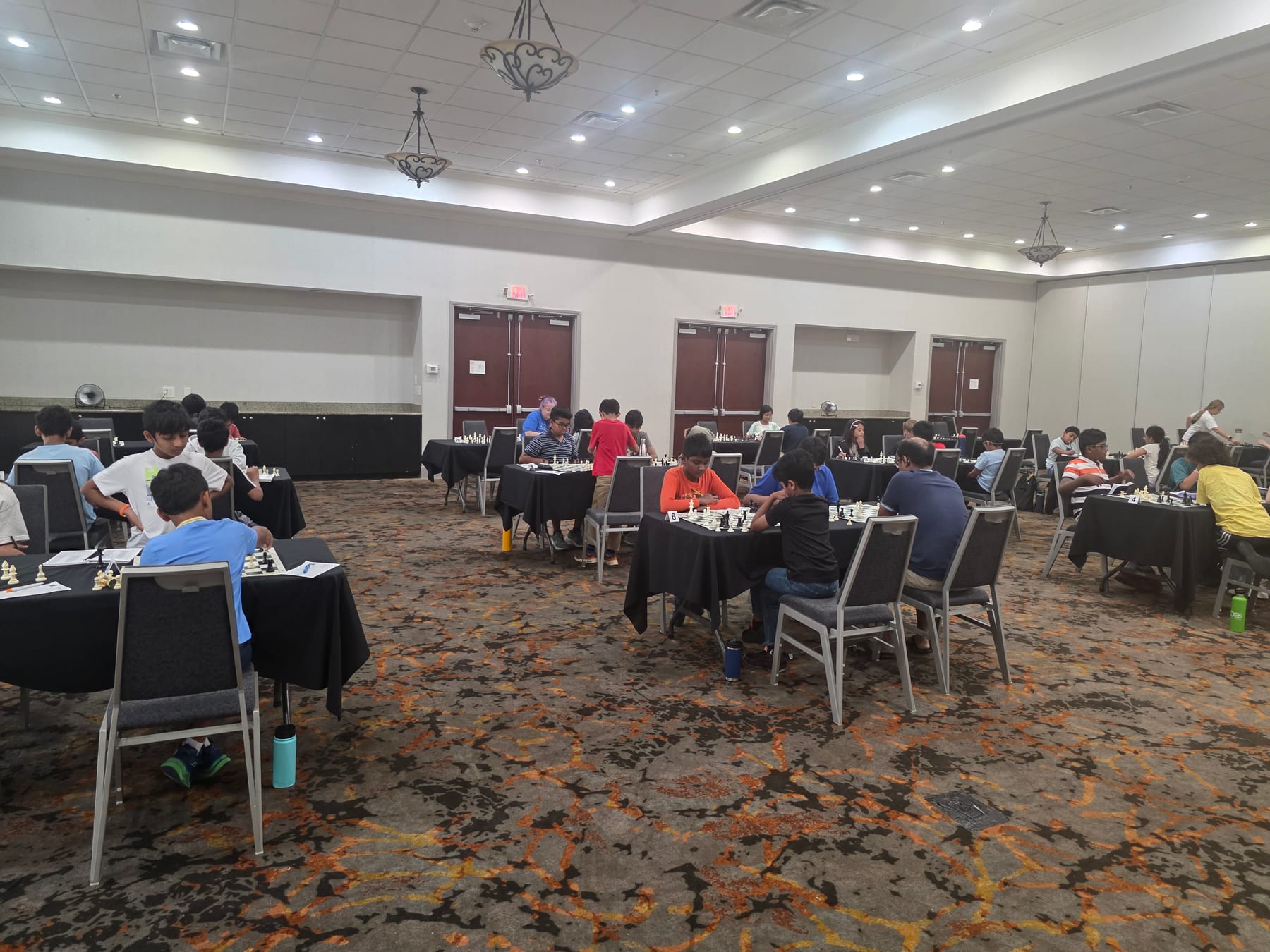 Players seated at chessboards across the Mohar tournament room.